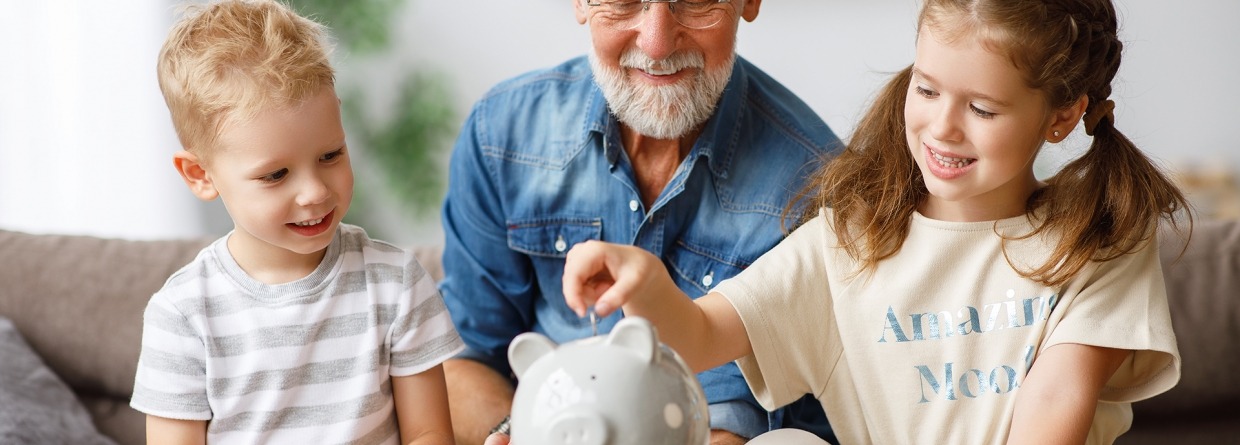 Een opa helpt twee kinderen met sparen en doet muntjes geld in een spaarvarken