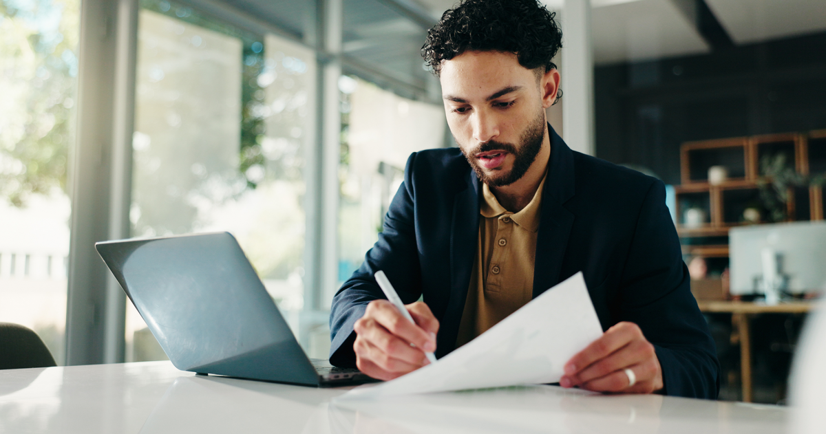 Man achter een bureau met laptop voor zich en een pen en document in zijn is een controle aan het uitvoeren